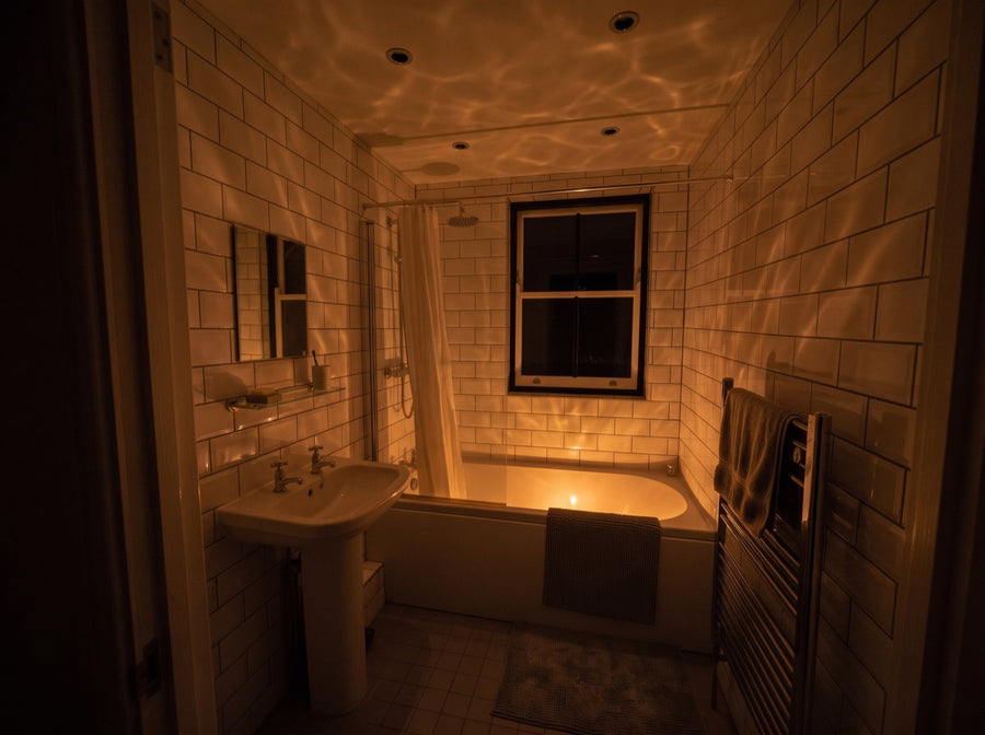 The same bathroom with the ceiling lights off, lit only by warm amber light and ripples across the ceiling