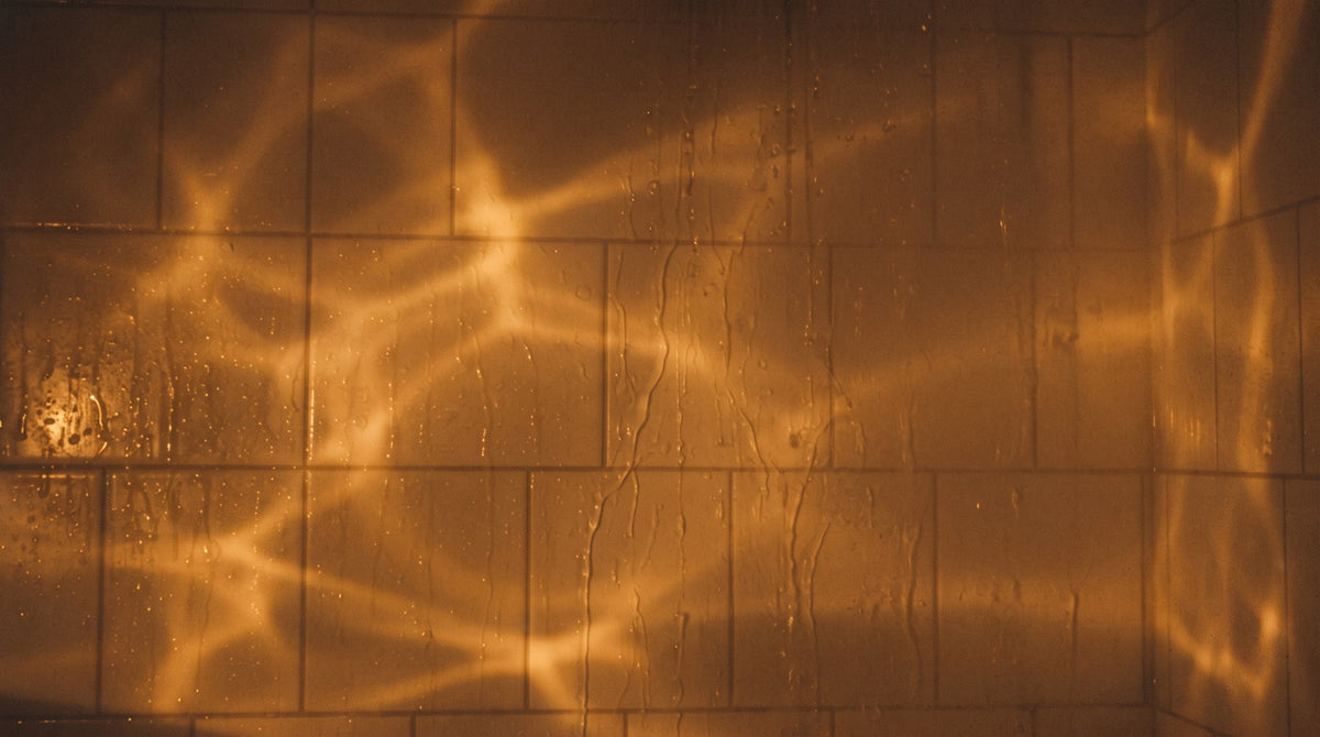 Wet white bathroom tile at night, warm amber ripples of light across it